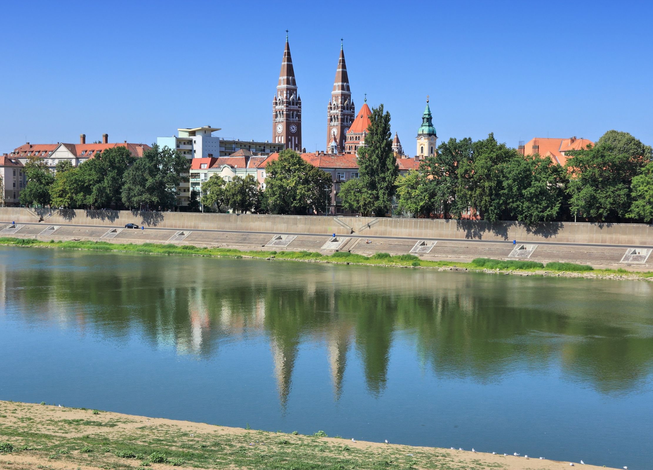 Stadtansicht mit Doppelturm-Kathedrale spiegelt sich im ruhigen Fluss vor blauem Himmel