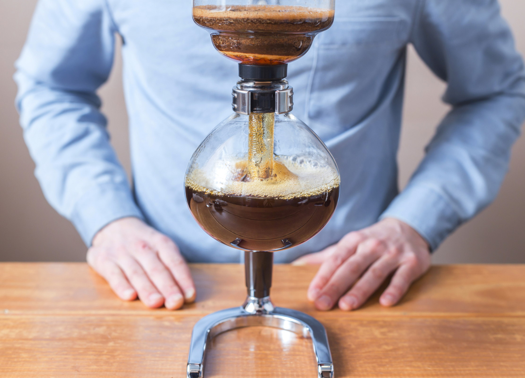 Gebrühter Kaffee fließt aus dem oberen Glasbehälter eines Syphon-Kaffeebereiters in die bauchige Glaskammer darunter
