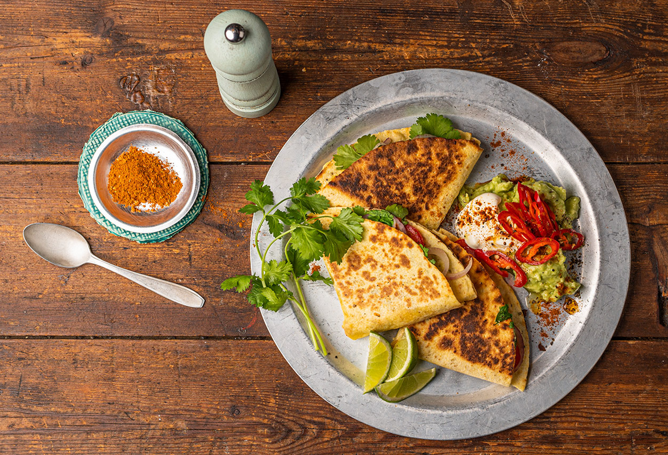 Gefaltete Quesadillas mit Avocado- und Bohnenmus auf einem Teller, daneben ein Löffel