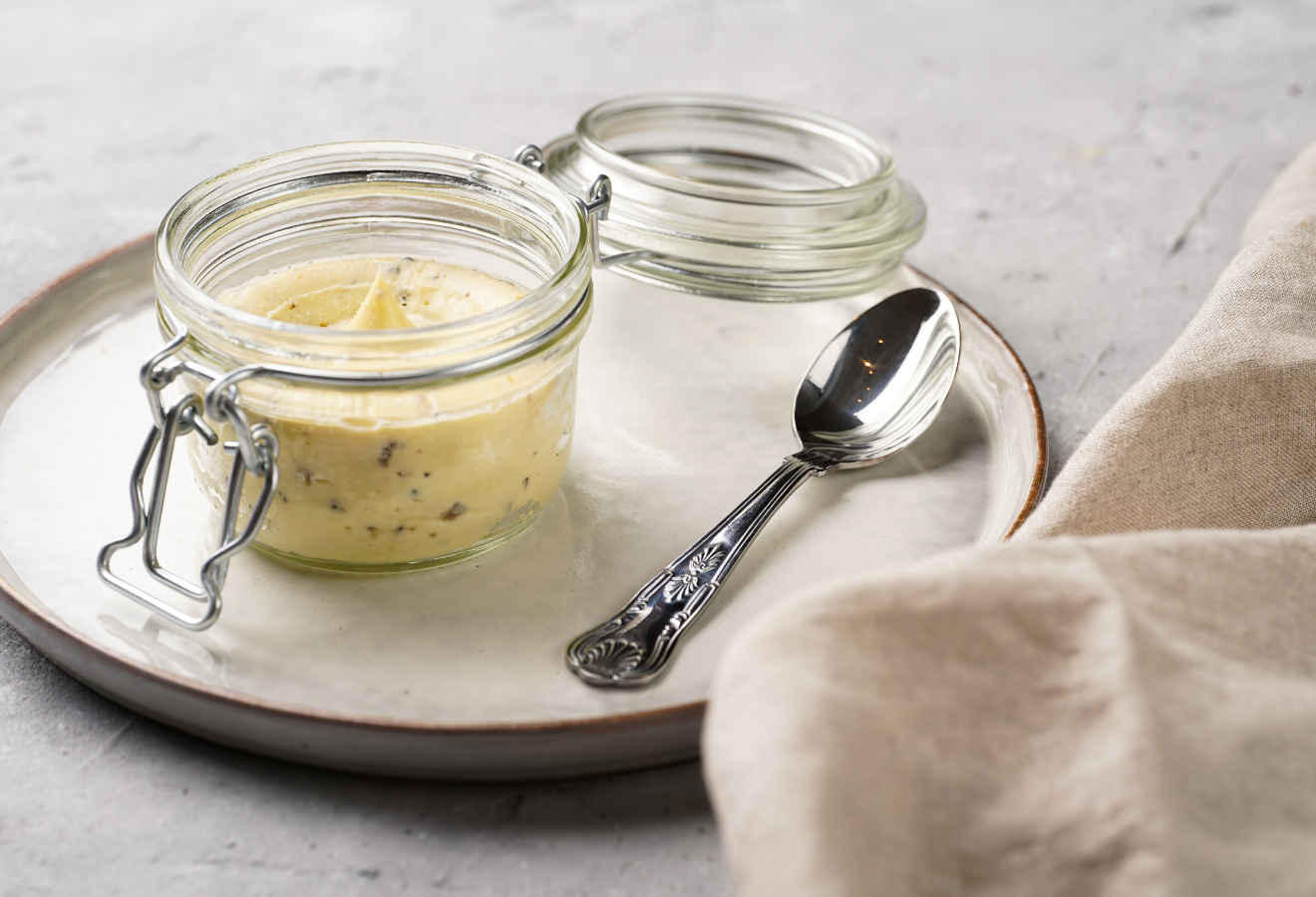Kräuterbutter in einem Einmachglas auf einem Teller mit einem Löffel daneben