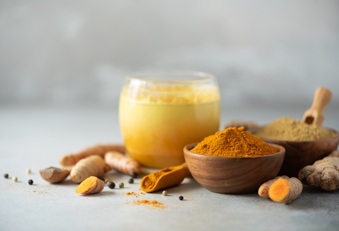 Goldene Milch in einem Glas, daneben Gewürze, Ingwerknollen und Kurkumaknollen
