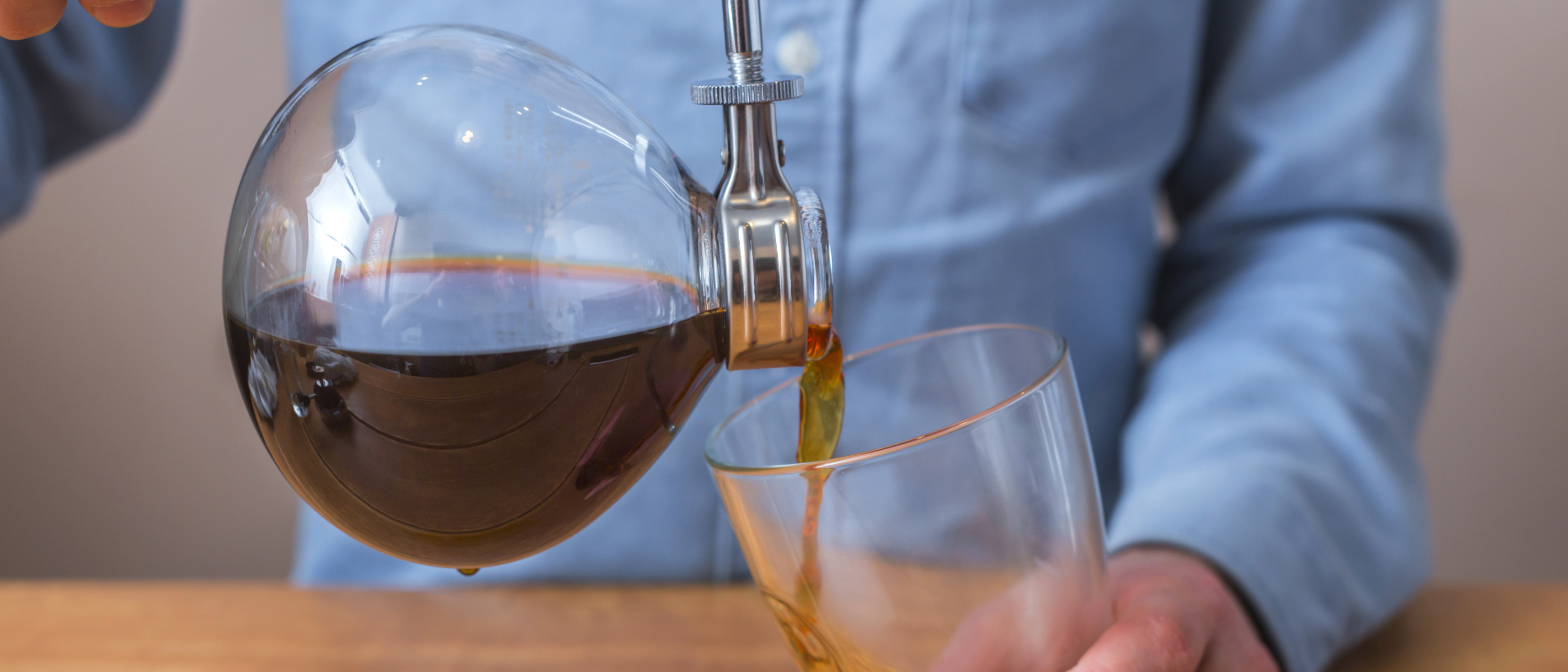 Frisch gebrühter Kaffee wird aus der Glaskammer eines Syphon-Kaffeebereiters in ein Glas eingeschenkt