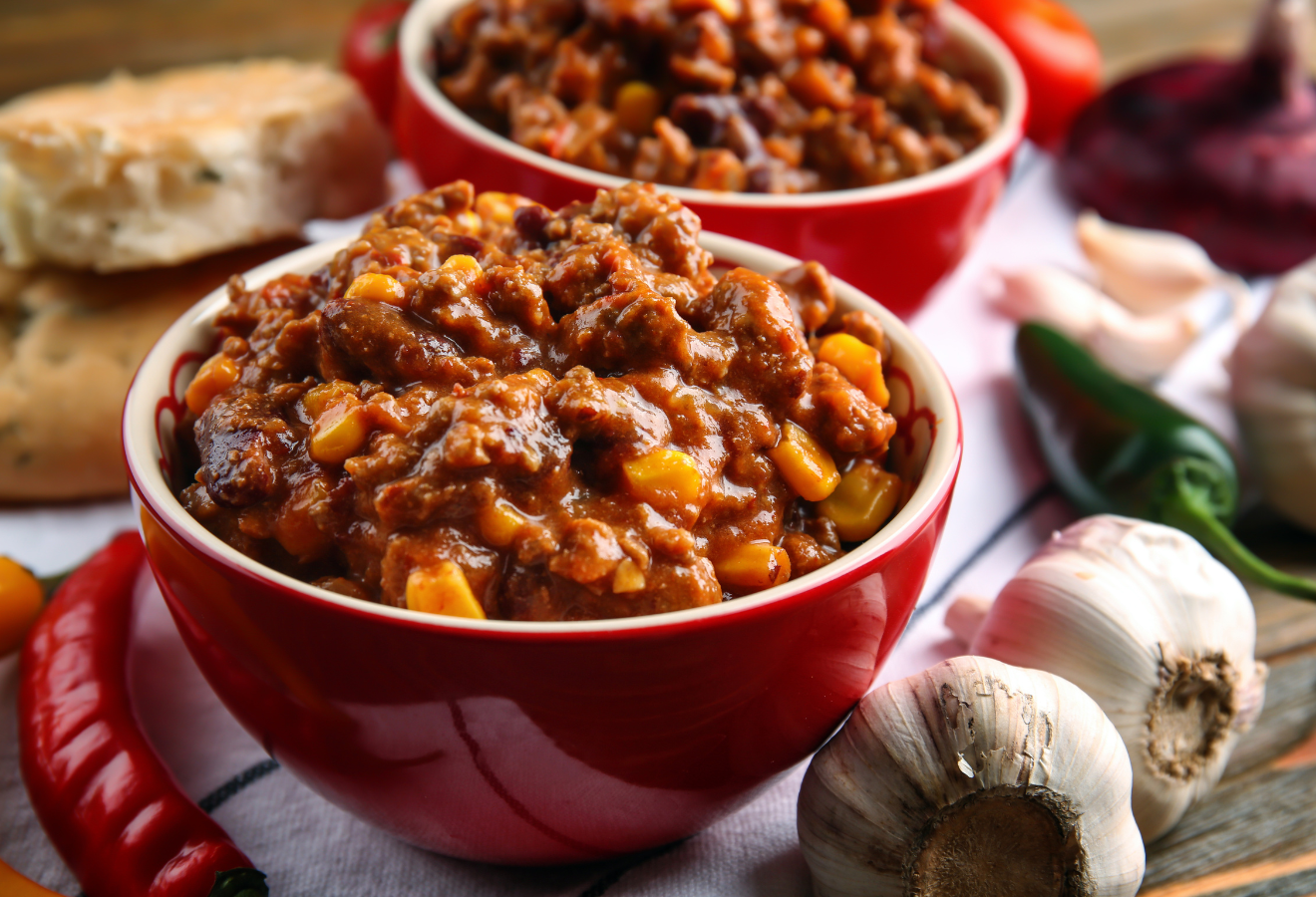 Chili con Carne, einfach, herzhaft, in 2 Schüsseln mit Knoblauch, Brot und Chilischoten daneben