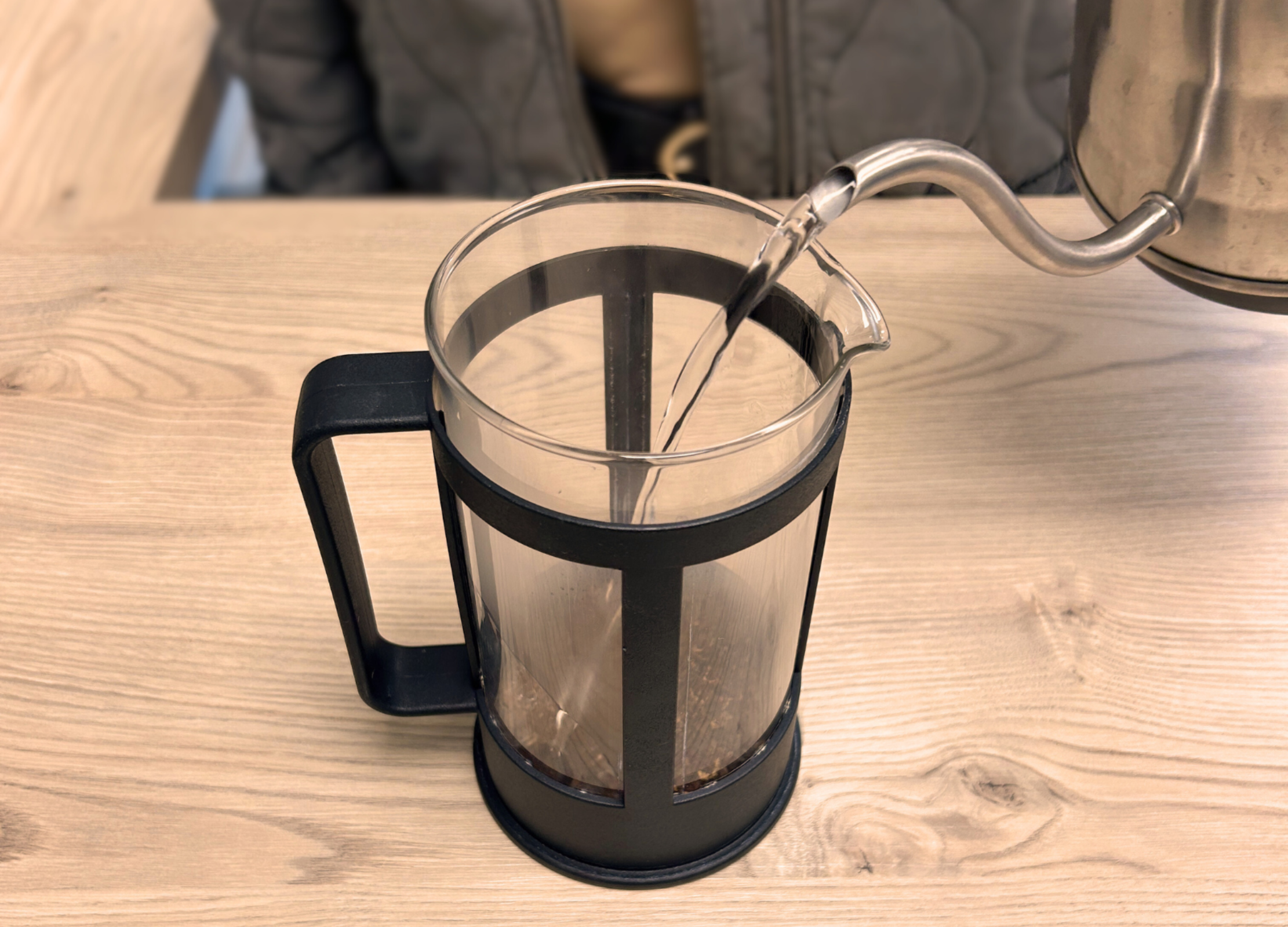 Wasser wird in einen French Press aus Glas mit gemahlenem Kaffee darin gefüllt