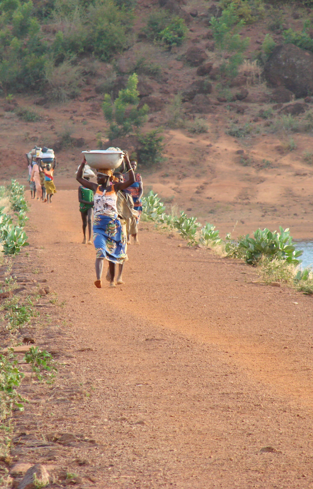 Menschen auf einem Sandweg die Wasserschalen auf dem Kopf tragen in Burkina Faso