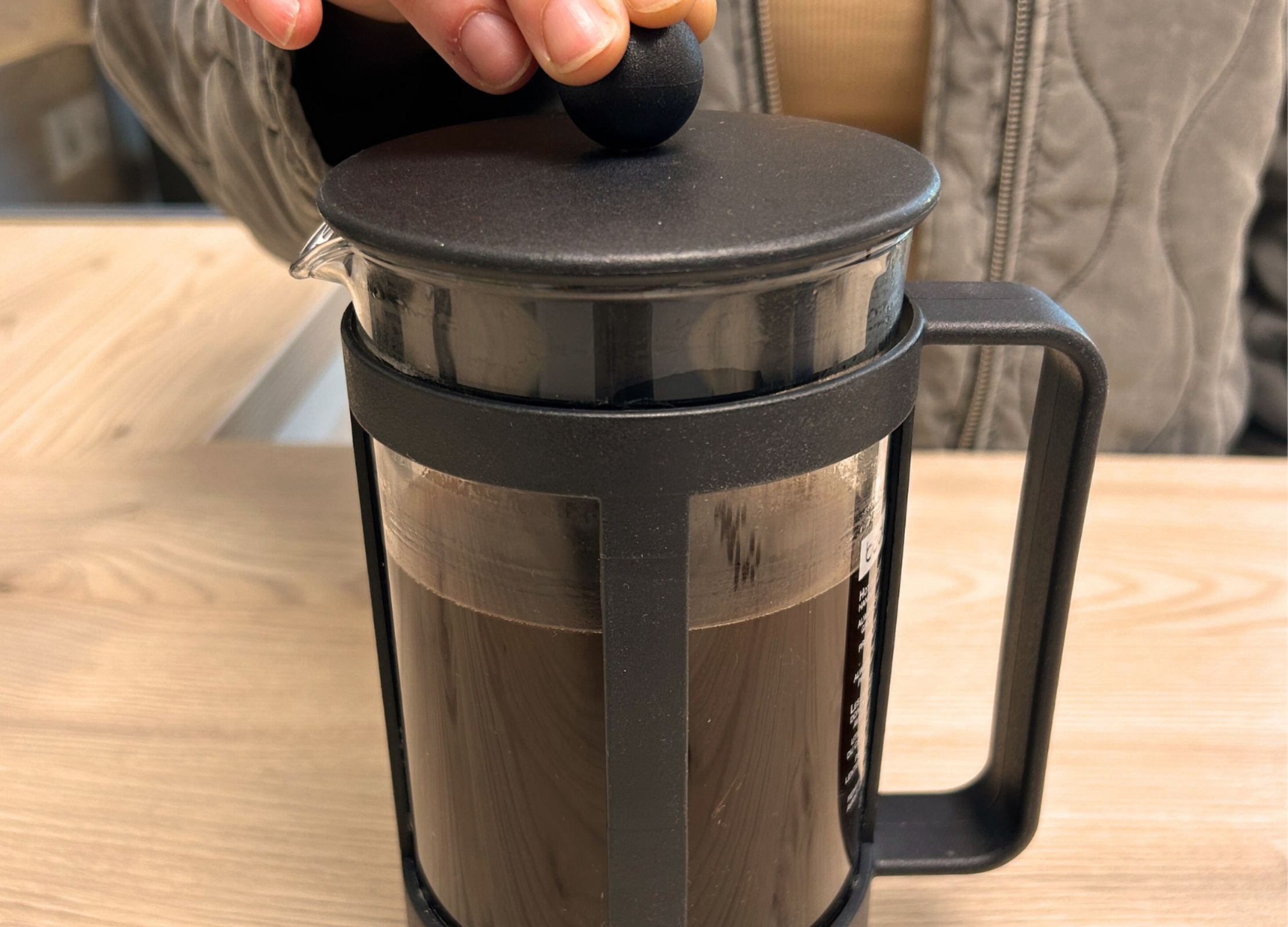 Eine Hand drückt den Deckel der French Press mit frisch aufgebrühtem Kaffee nach unten