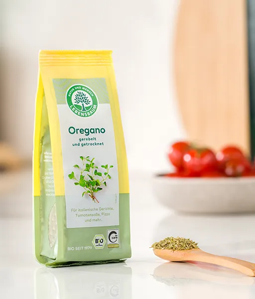Kategoriebild für Kräuter und Kräutermischungen von LEBENSBAUM, Oregano-Verpackung auf einer Küchenzeile neben einem Löffel mit getrockentem Oregano