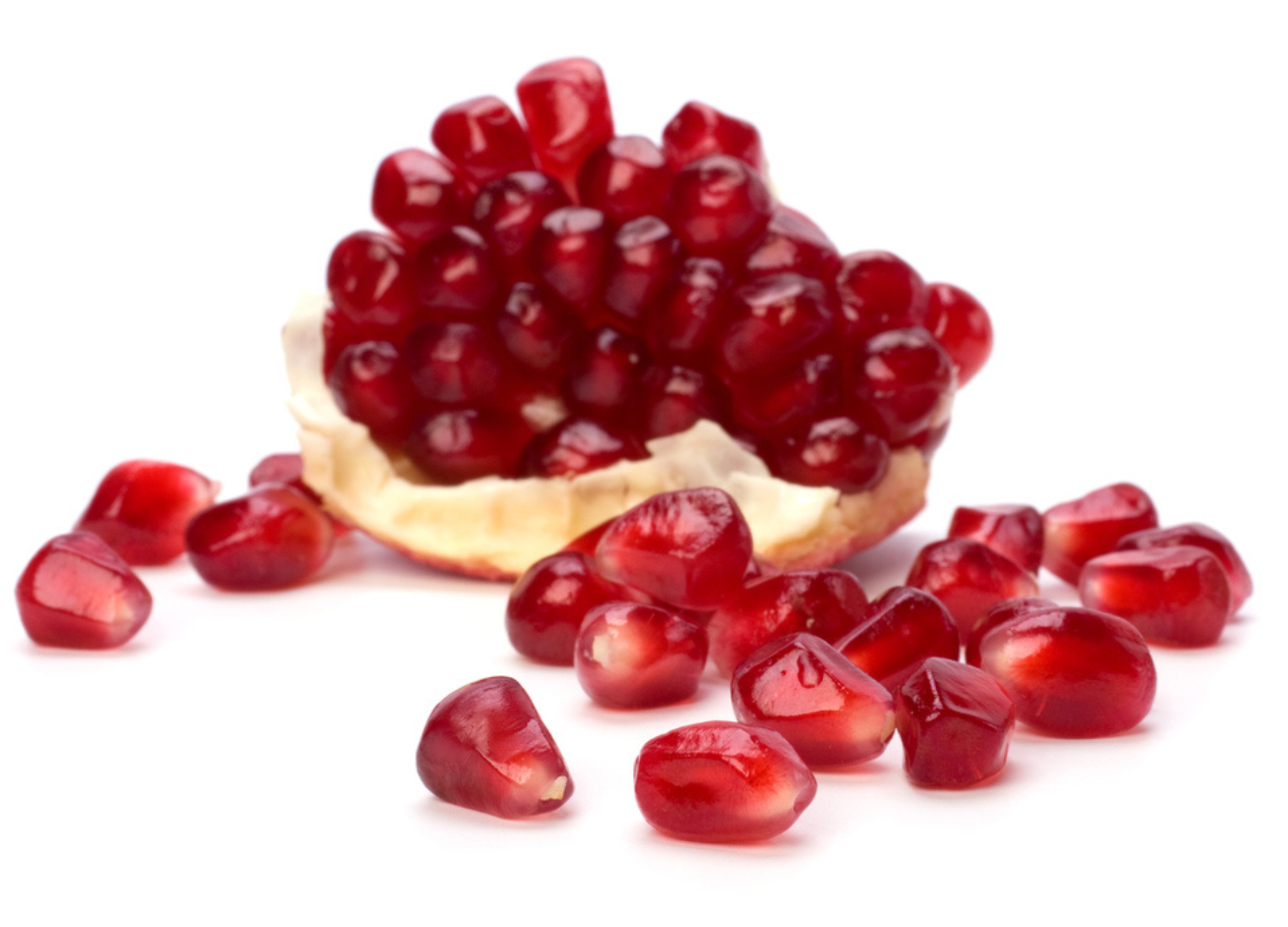Granatapfel Rote Granatapfelkerne liegen auf einer weißen Oberfläche, einige noch in einem Stück der Fruchtschale
