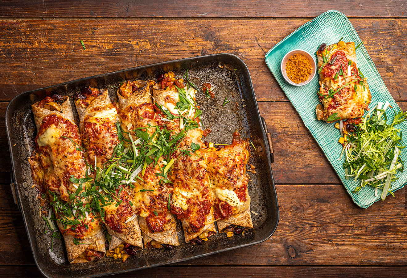 Enchilada Verdura auf einem Blech angerichtet, mit Käse überbacken, daneben ein Teller mit Salat