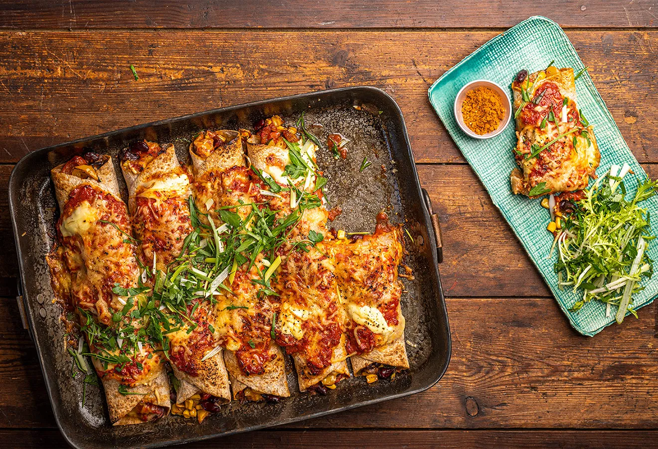 Enchilada Verdura auf einem Blech angerichtet, mit Käse überbacken, daneben ein Teller mit Salat