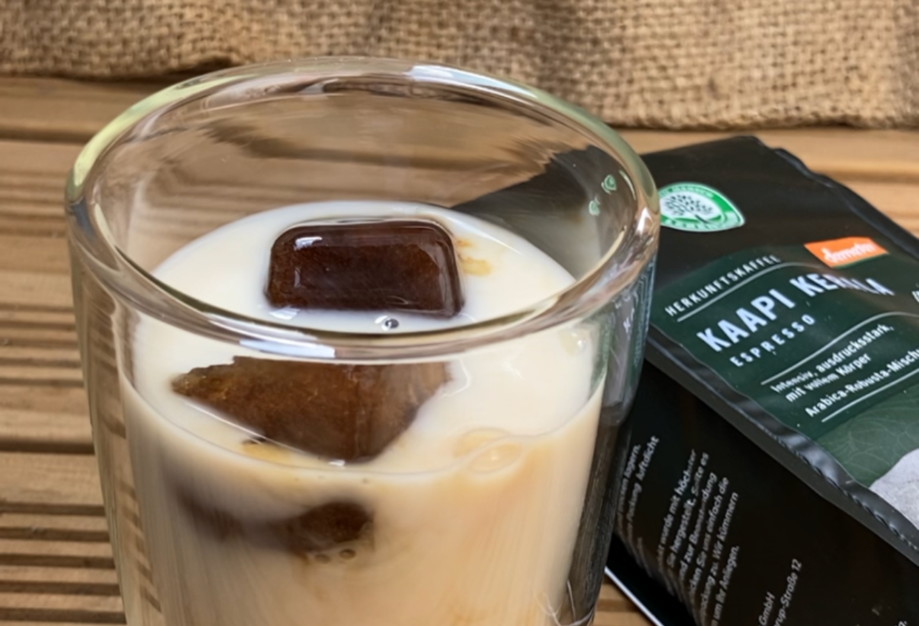 Espressowürfel mit Milch in einem Glas, im Hintergrund eine Packung Kaapi Kerala Kaffee