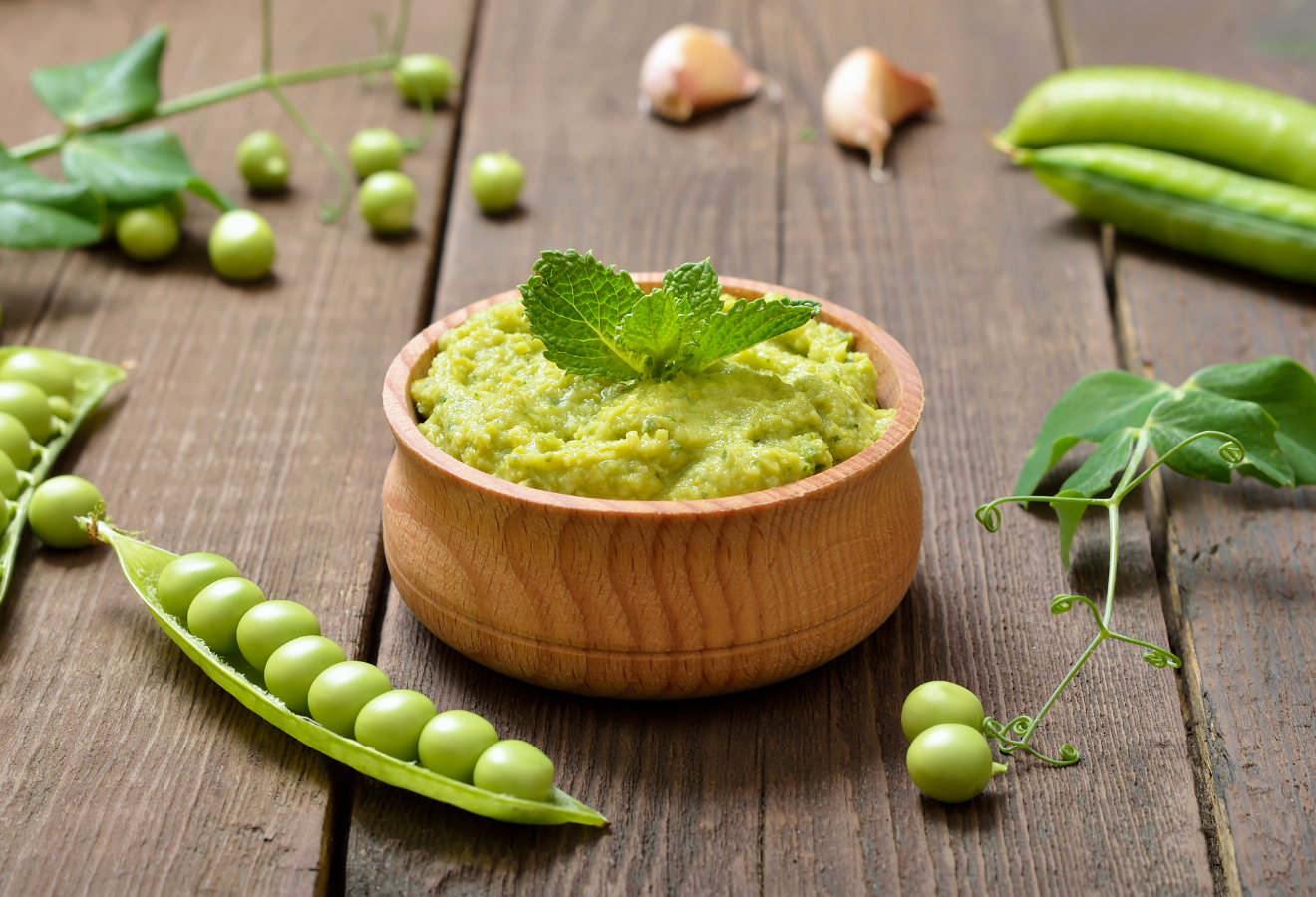 Grüner Dip in einem Holzsschälchen, daneben Erbsen und Erbsenbohnen
