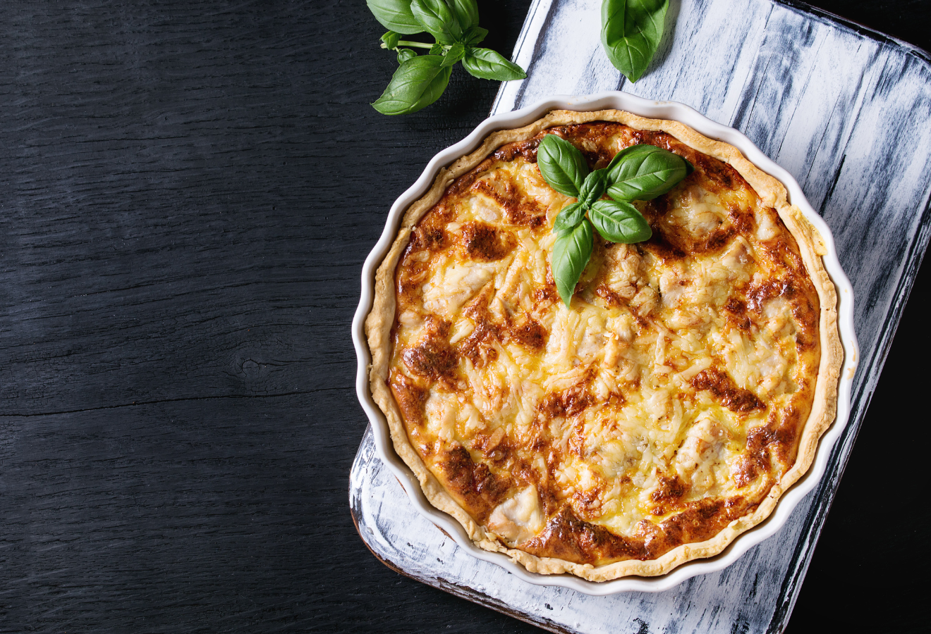 Schwarzwurzelquiche mit Schalotten und Salbei in einer Quicheform auf einem Holzbrett, mit Basilikum angerichtet