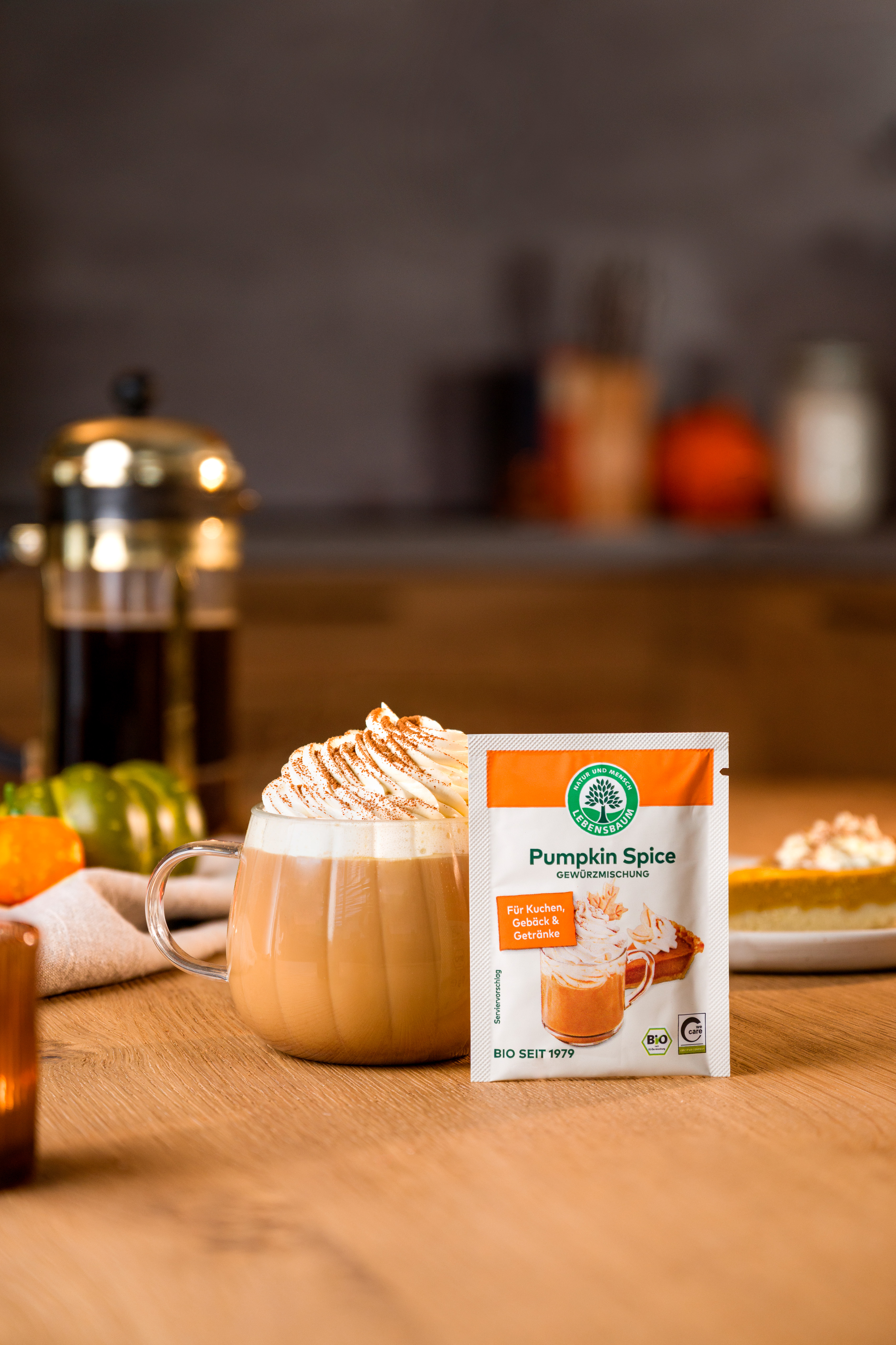 Pumpkin Spice Gewürzmischung neben einem Pumpkin Spice Latte mit Sahne auf einem herbstlich dekorierten Tisch