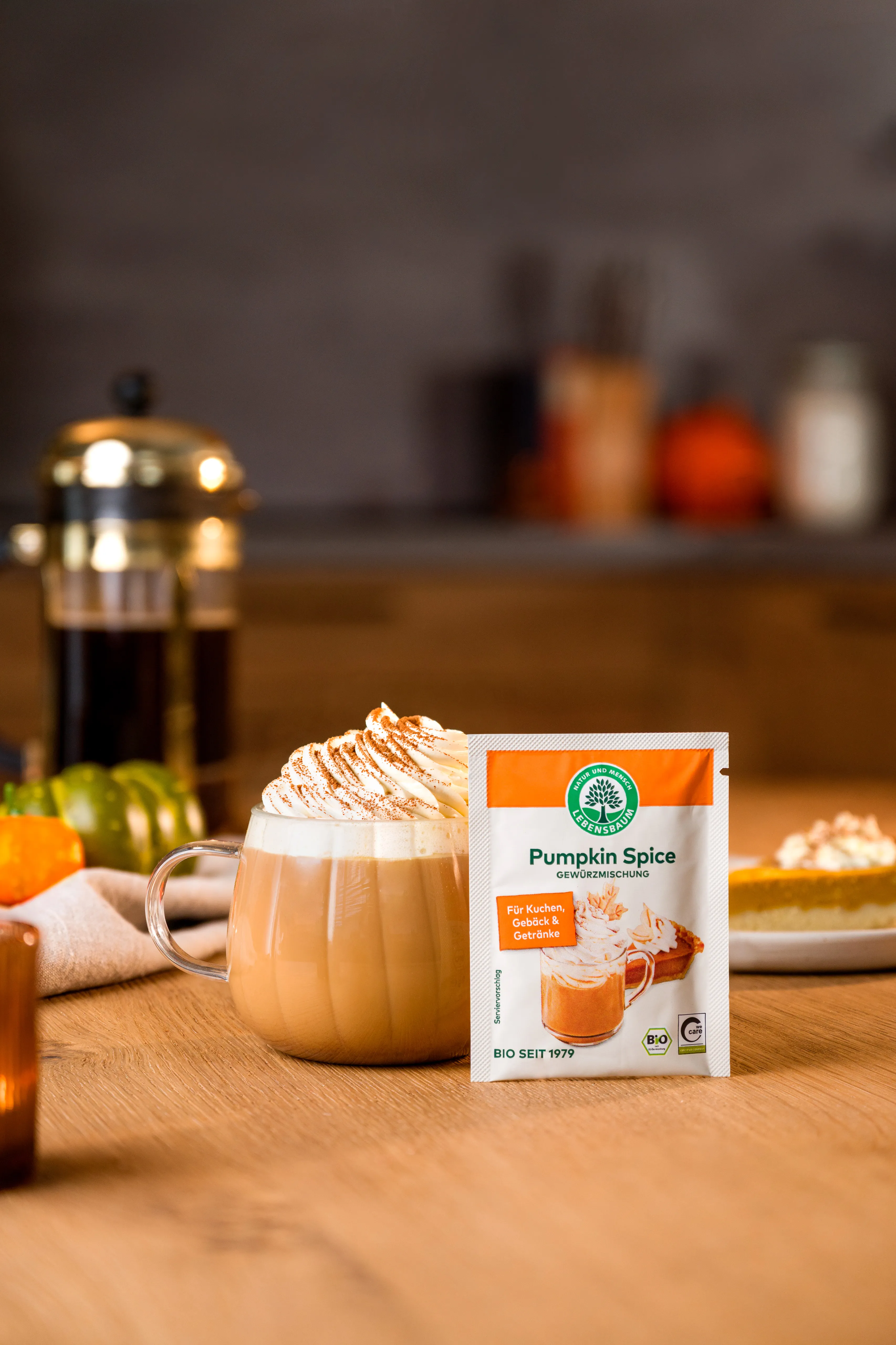 Pumpkin Spice Gewürzmischung neben einem Pumpkin Spice Latte mit Sahne auf einem herbstlich dekorierten Tisch