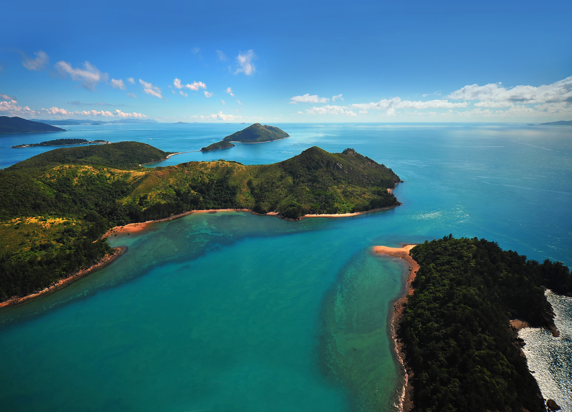 Grüne Inseln mit bewaldeten Hügeln in türkisblauem Meer unter blauem Himmel in Australien