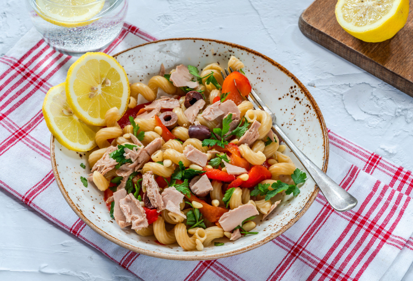 Mediterraner Nudelsalat in einer Schale mit Zitronenscheiben angerichtet und einer Gabel darin