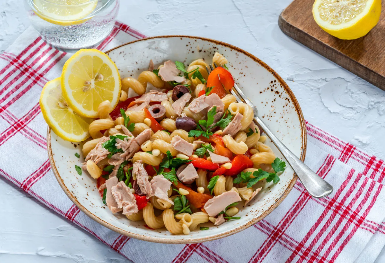 Mediterraner Nudelsalat in einer Schale mit Zitronenscheiben angerichtet und einer Gabel darin