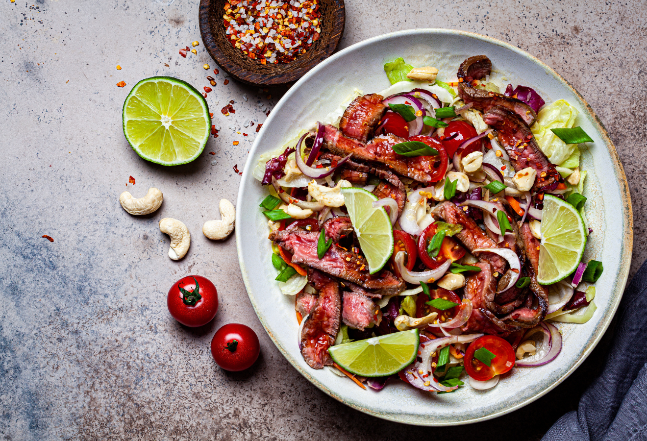 Thai-Roastbeef-Salat auf einem weißen Teller mit Limettenspalten
