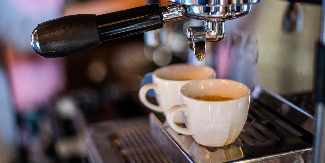Zwei kleine weiße Espressotassen stehen auf der Tassenablage einer Siebträgermaschine