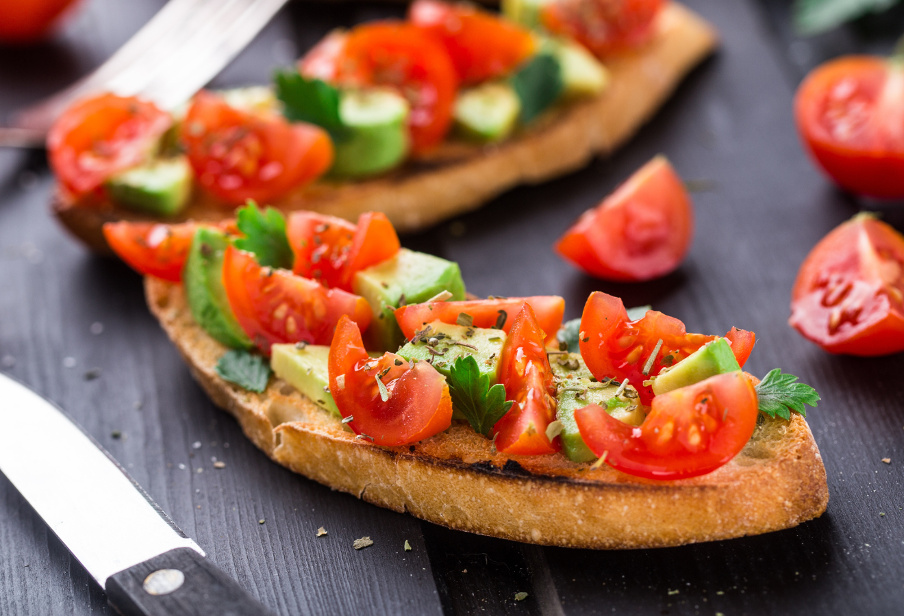 Bruschetta mit Avocado und Koriander, Tomaten im Hintergrund