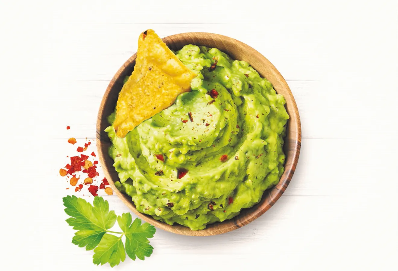 Guacamole in einer Holzschale mit einem Tortillachip darin