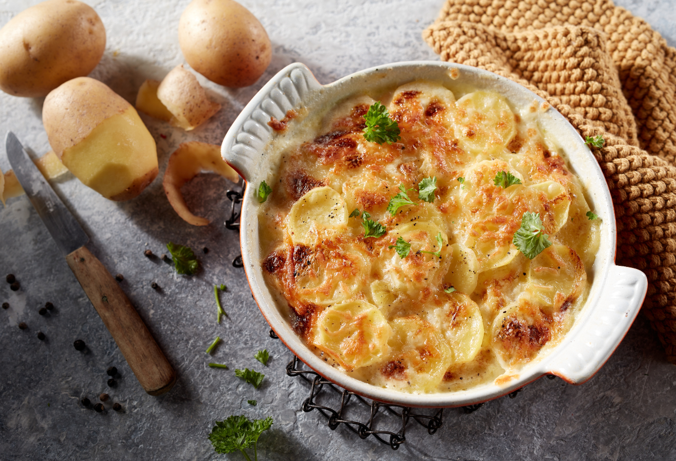 Wirsing-Kartoffel-Gratin in einer weißen Auflaufform daneben Kartoffeln