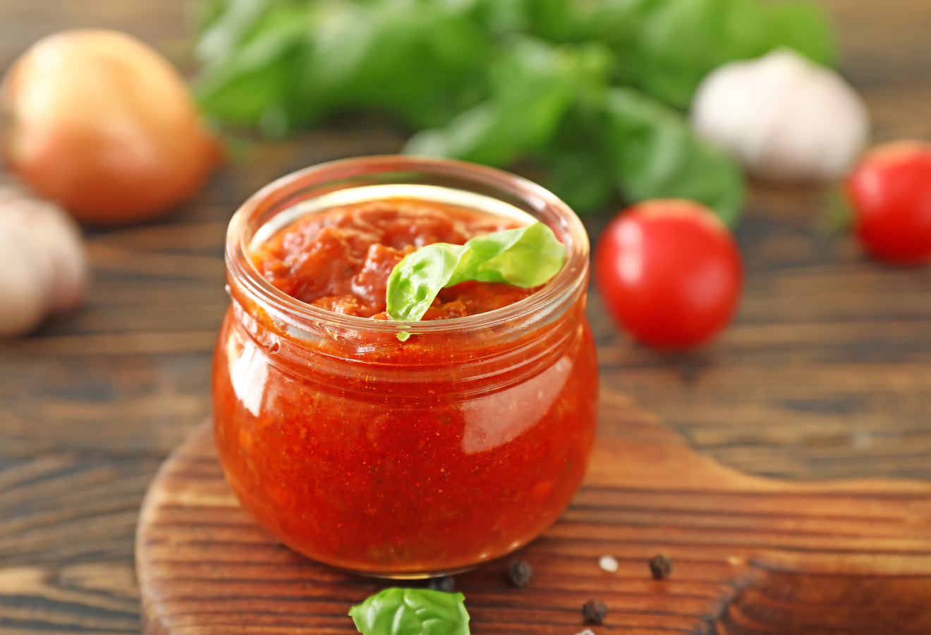 Tomaten-Ketchup in einer Glasschale auf einem Holzbrett mit Basilikum garniert