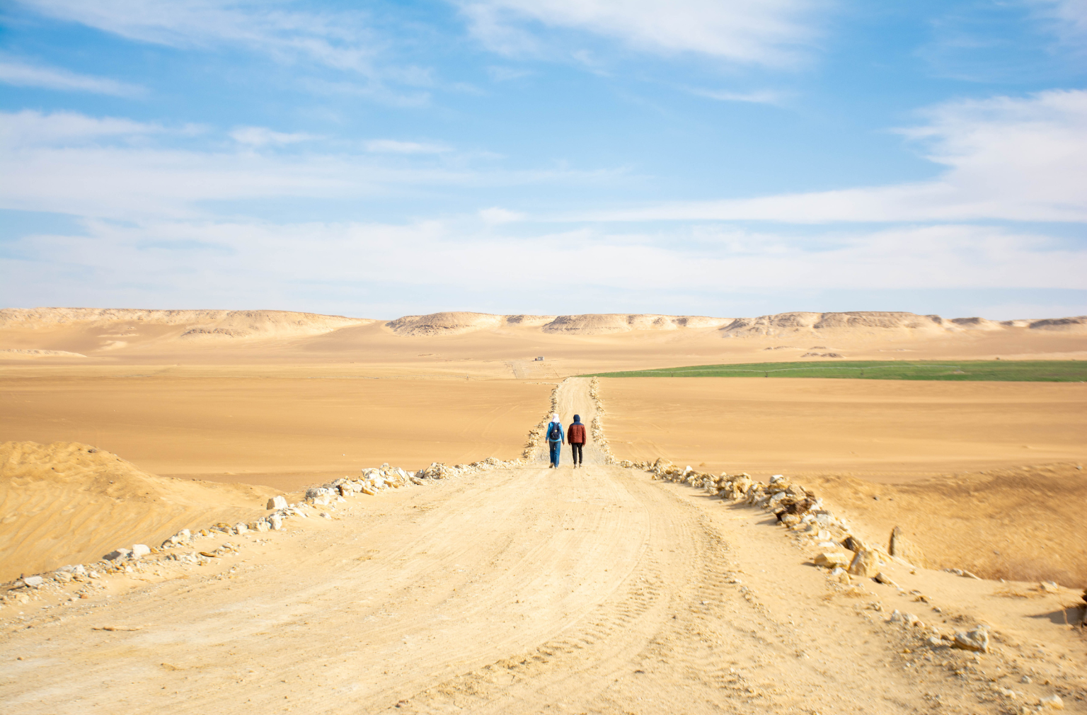 Wüste mit einer Sandstraße, darauf zwei Menschen in Ägypten