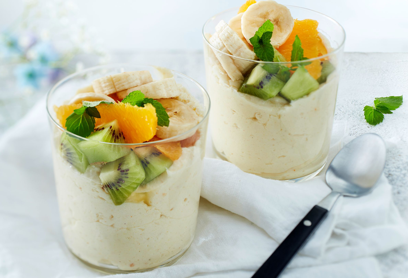 Kurkuma-Orange-Dessertmousse mit Obstsalat in zwei Gläsern, daneben ein Löffel