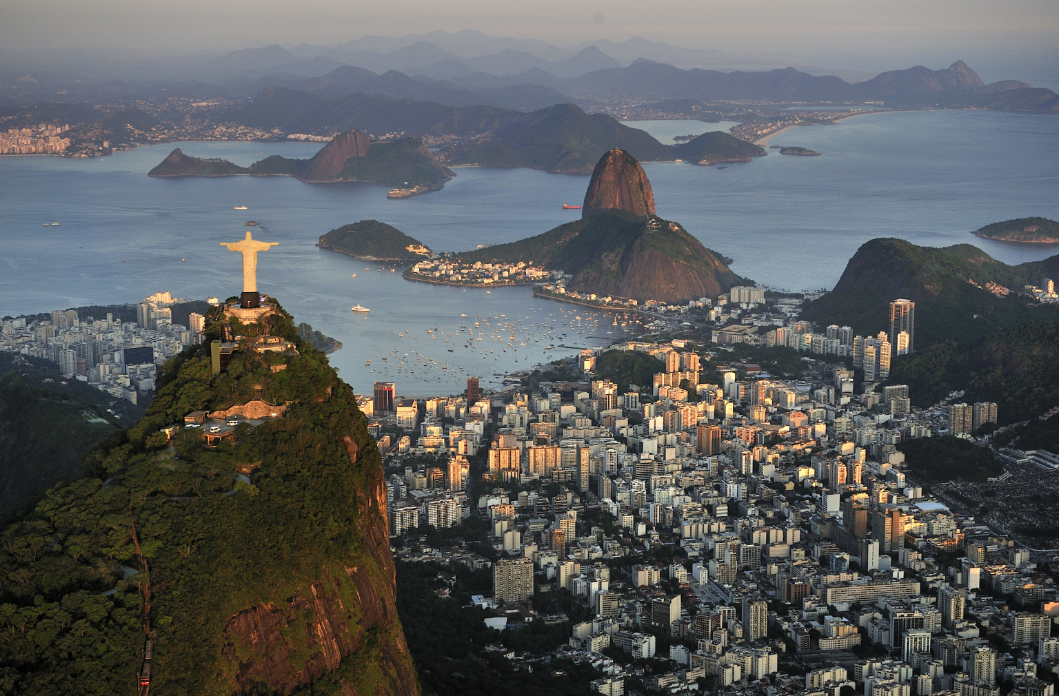 Panoramablick auf Rio de Janeiros Küste mit Christusstatue auf einem Hügel und markantem Felsen im Meer