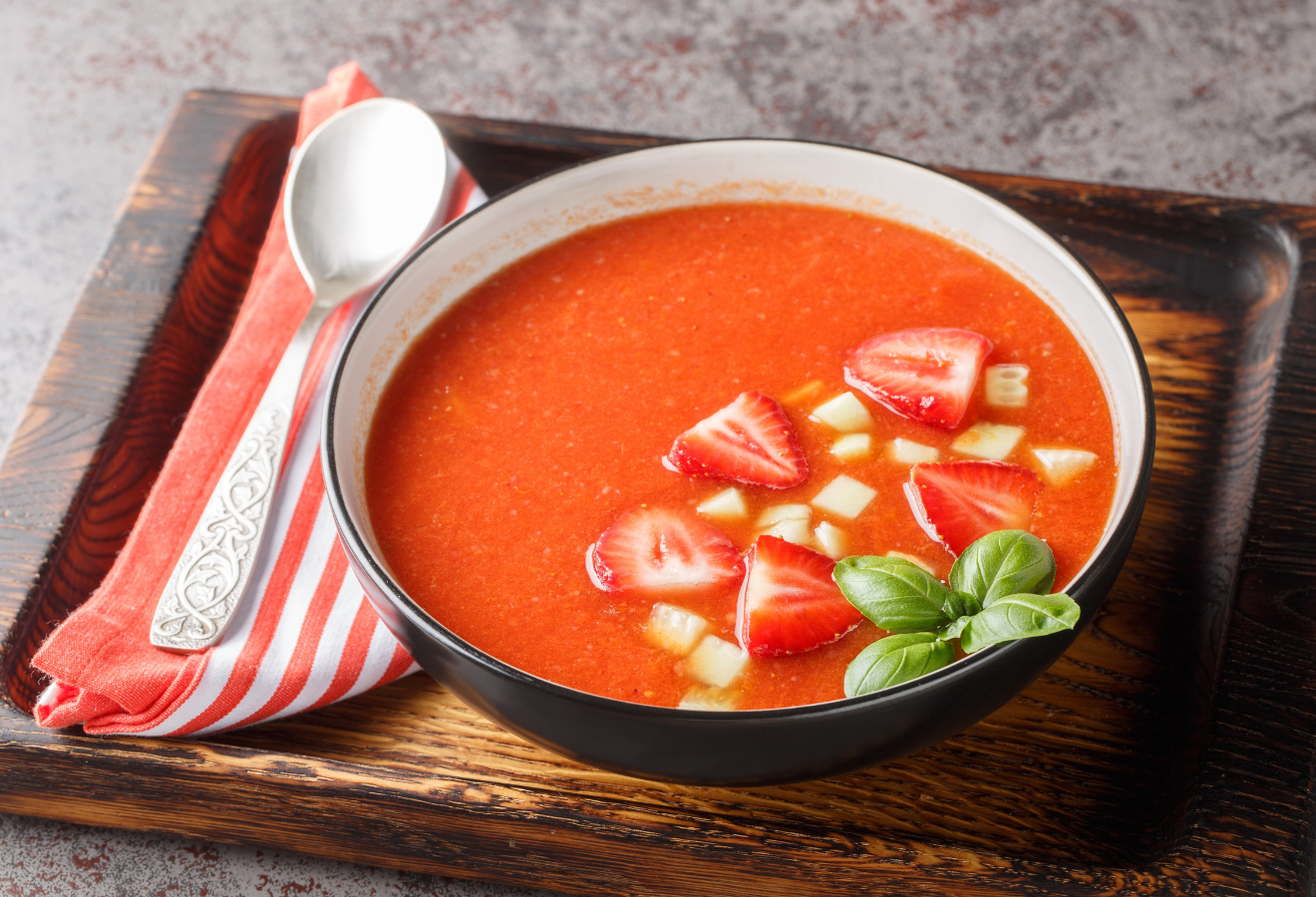 Erdbeer-Tomaten-Gazpacho in einer schwarzen Schüsseln mit einem Löffel daneben