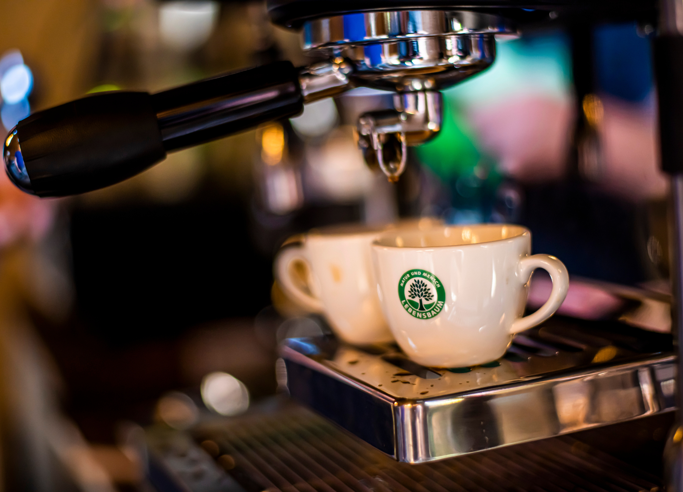 Zwei weiße Tassen mit Lebensbaum Logo stehen unter einer Espressomaschine, bereit zum Befüllen