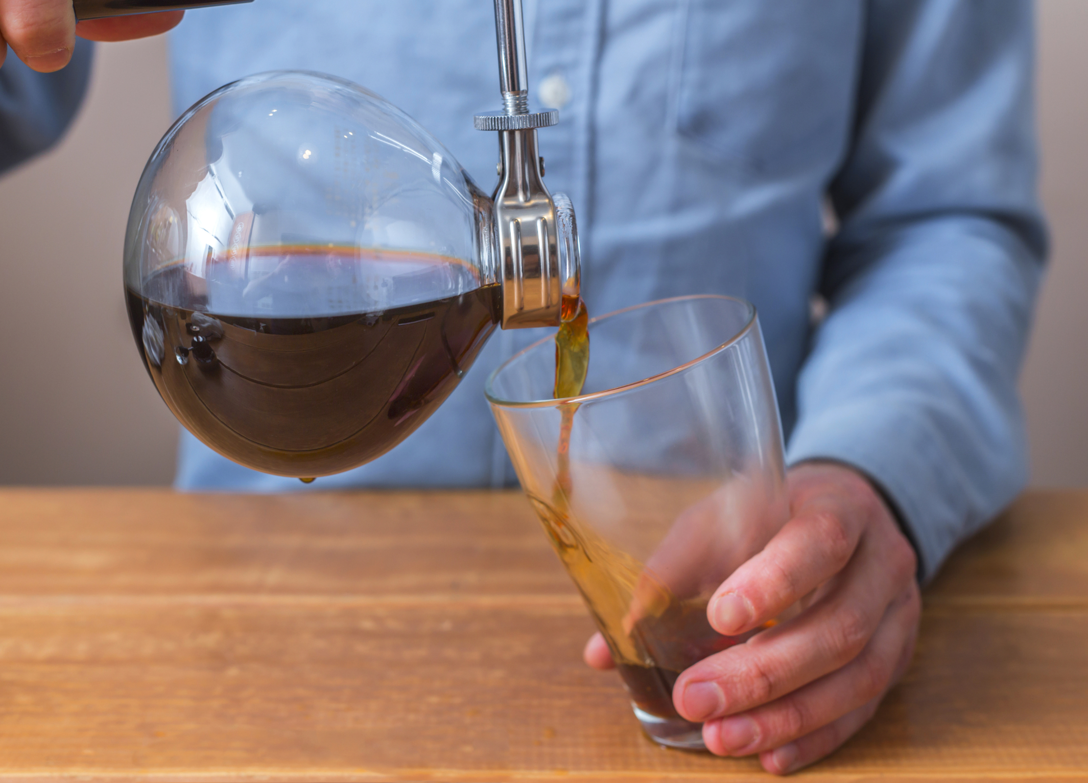 Frisch gebrühter Kaffee wird aus der Glaskammer eines Syphon-Kaffeebereiters in ein Glas eingeschenkt