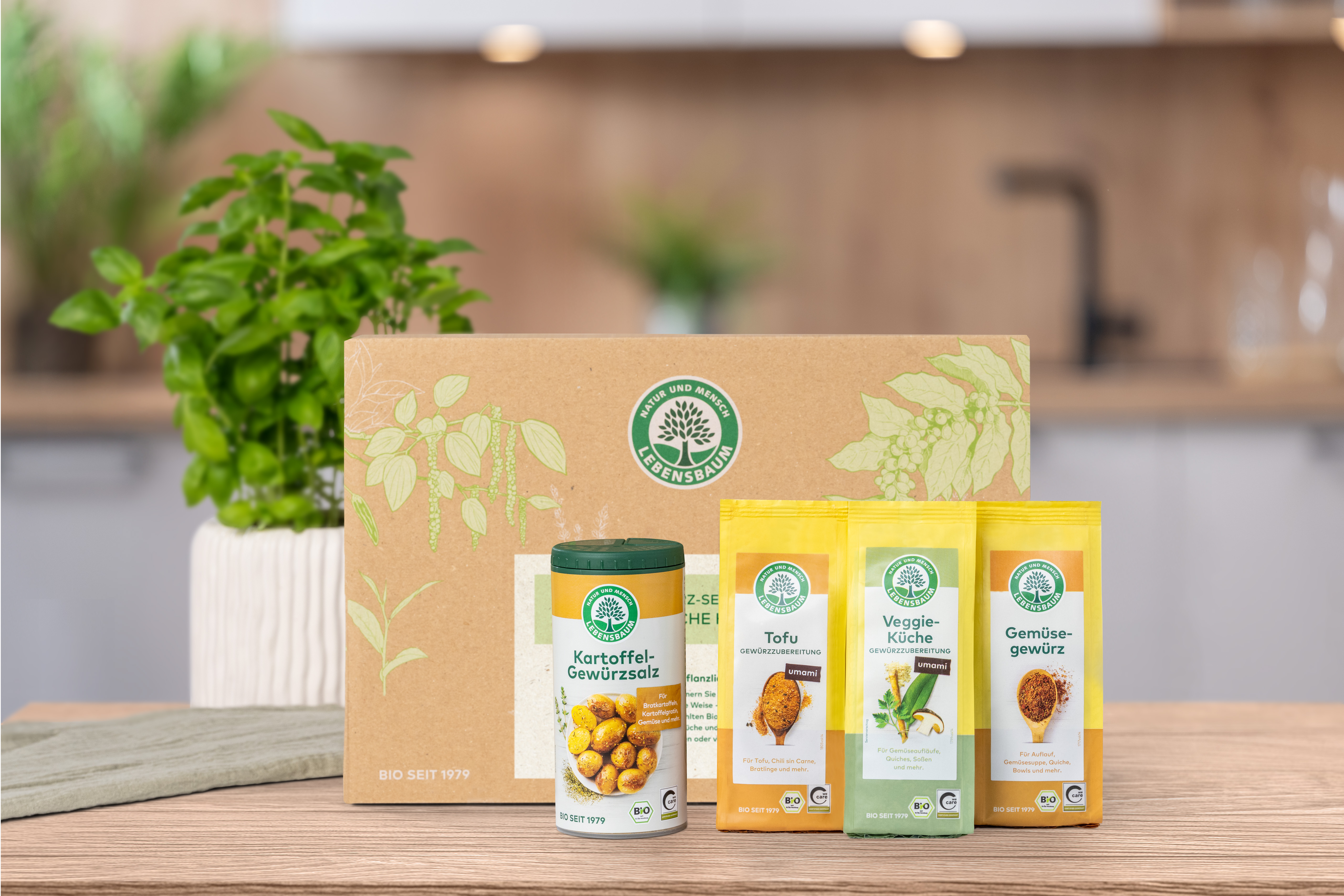 Verschlossenes Geschenk-Set steht auf einem Holztisch in der Küche. Vor der Geschenk-Set Verpackung  stehen die darin enthaltenen Produkte