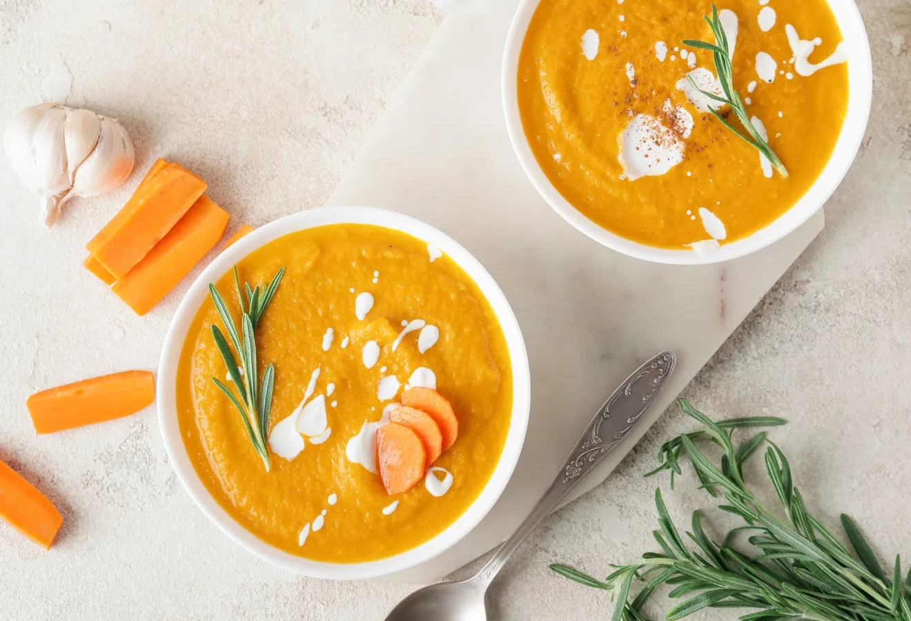 Möhrencremesuppe in zwei weißen Schüsseln mit Möhrenscheiben, Sahne und Rosmarin garniert