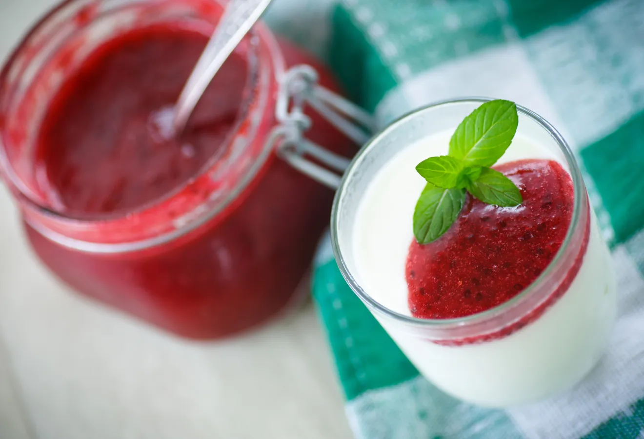 Panna cotta mit Granatapfelsirup in einem Glas mit Minzblättern garniert