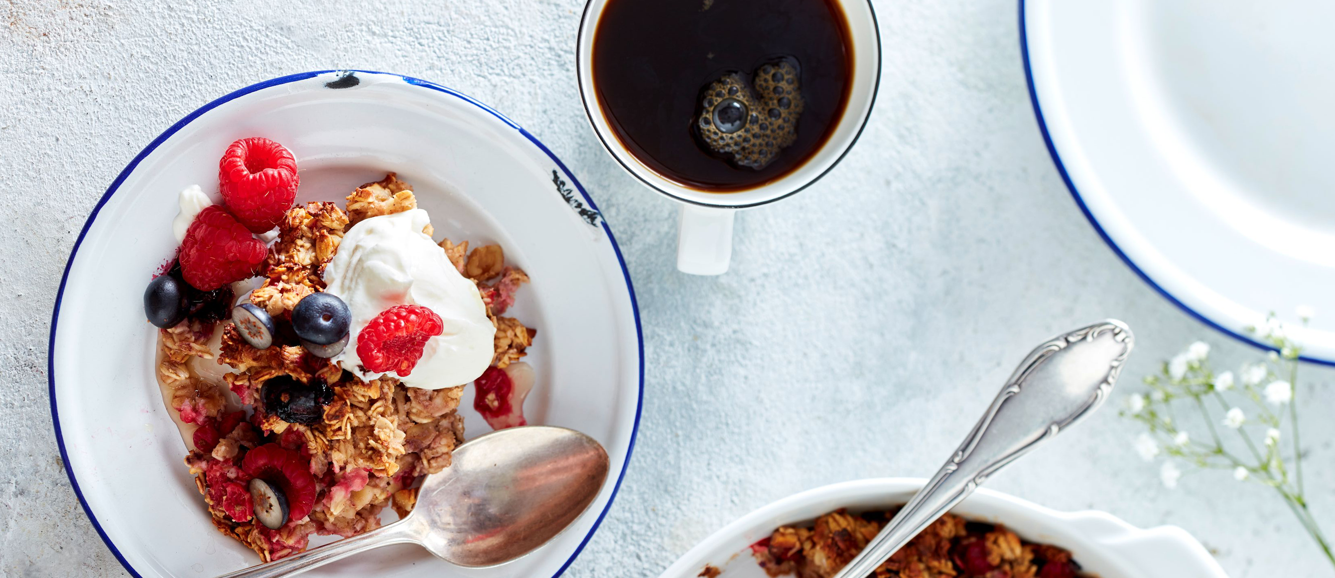 Frühstücksgranola mit Beeren in einer weißen Schüssel, daneben eine Tasse mit Kaffee