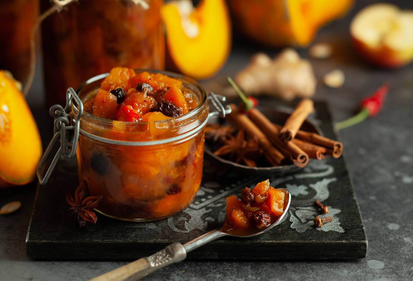 Kürbisrelish in einem Einmachglas, daneben Zimtstangen und ein Löffel