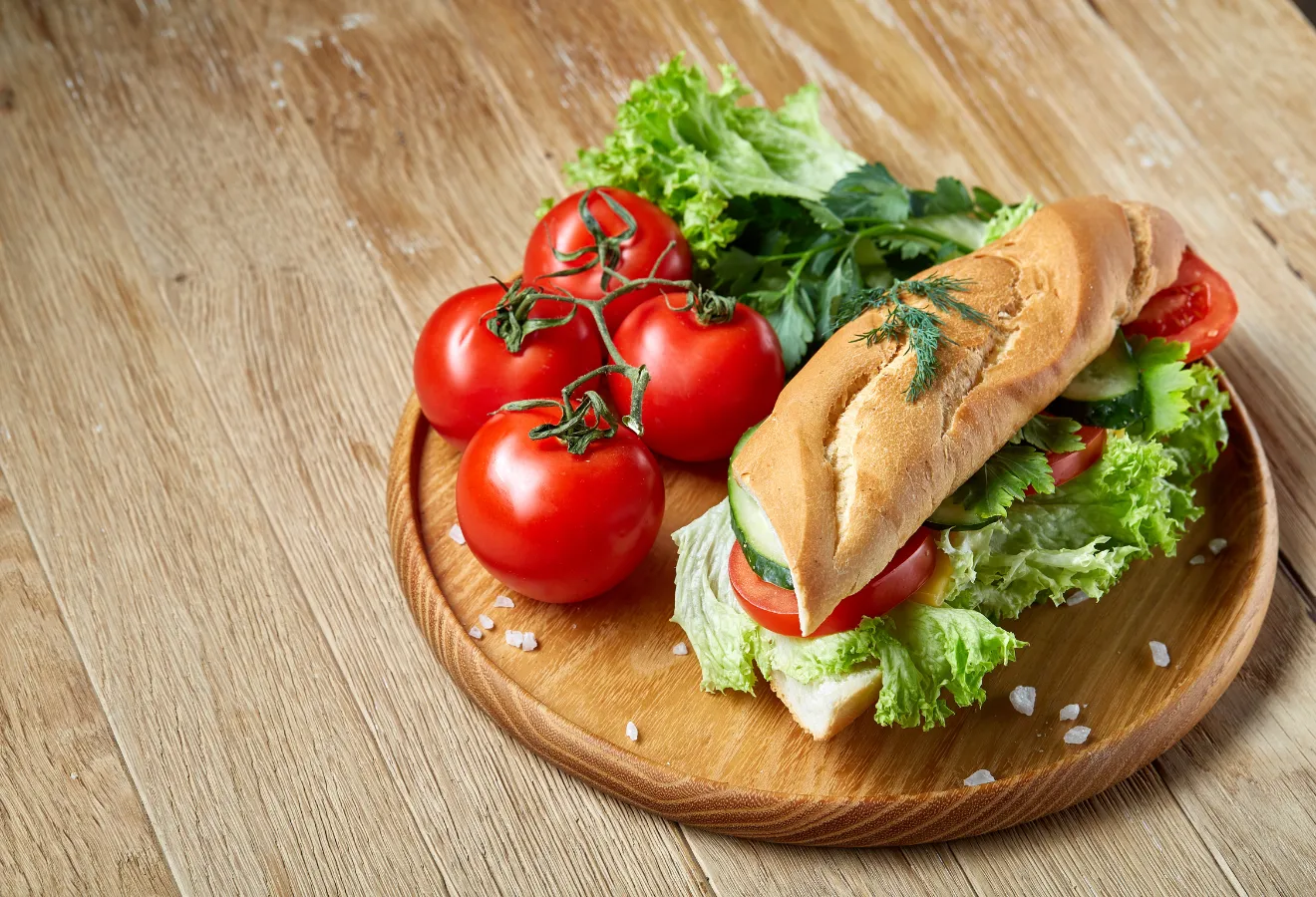 Baguette mit Hähnchen und Käse auf einem Teller mit Tomaten und Salat angerichtet