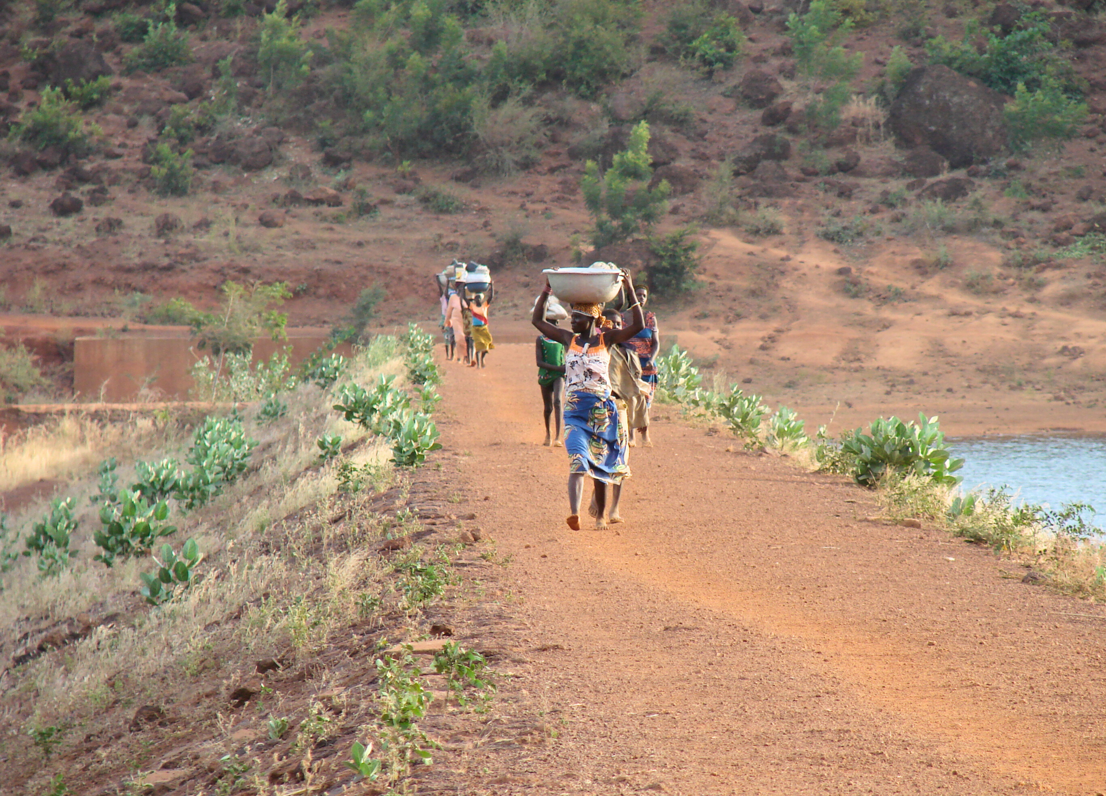 Menschen tragen Lasten auf einem Weg durch trockene Hügellandschaft in Burkina Faso