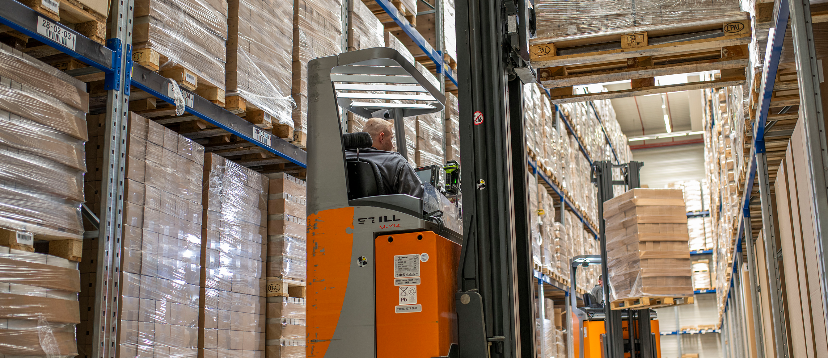 Lagermitarbeiter auf einem Gabelstapler zwischen Regalen