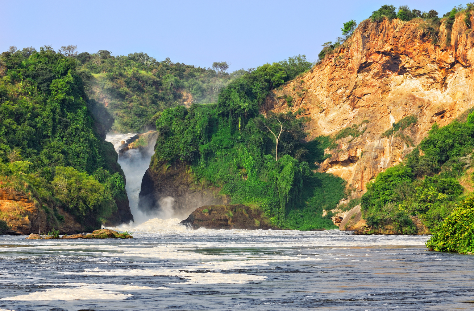 Wasserfall zwischen grünen Felsen, mündend in einen breiten Fluss in Uganda
