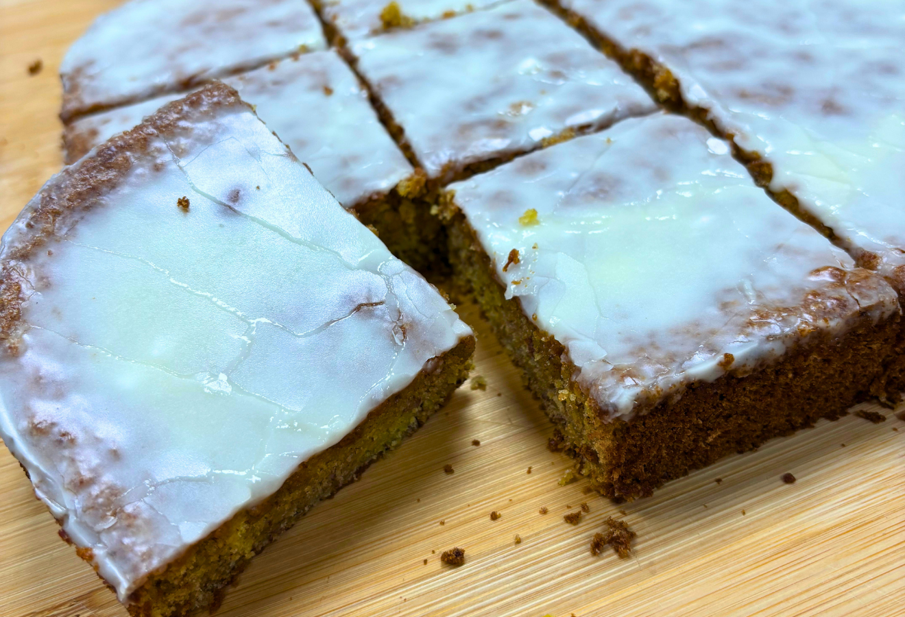 einige Stücke Möhrenkuchen mit Zuckerglasur liegen auf einem Holzbrett