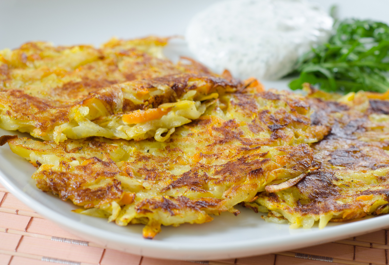 Bunte Frühlingsrösti mit grüngetupftem Kräuterquark, daneben Kräuter auf einem Teller