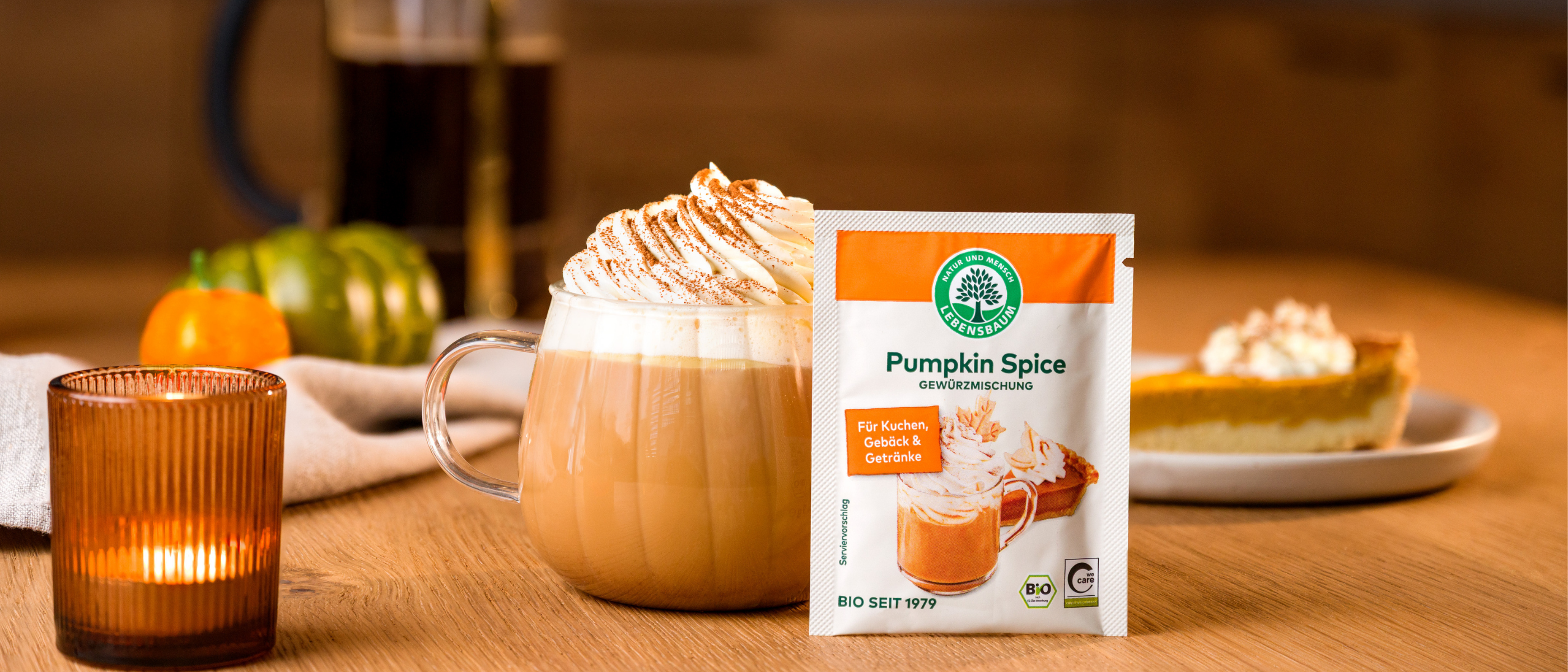 Pumpkin Spice Gewürzmischung neben einem Pumpkin Spice Latte mit Sahne auf einem herbstlich dekorierten Tisch