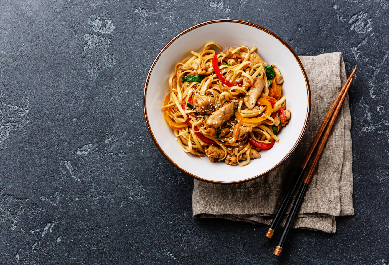Wok „Asia Style“ in einer weißen Schale, daneben Essstäbchen