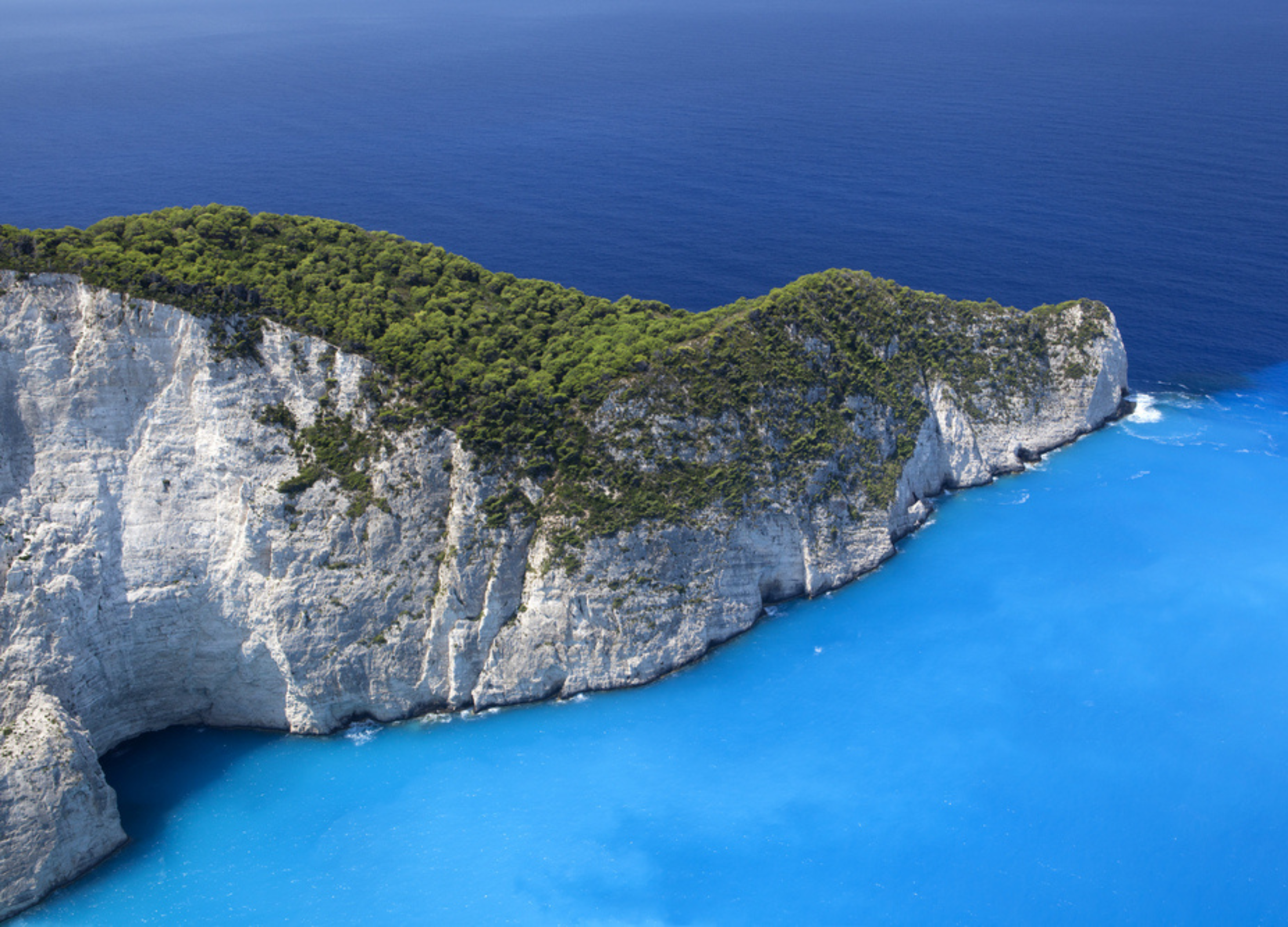 Weiße Steilküste mit dichtem Wald, umgeben von tiefblauem und türkisfarbenem Meer in Griechenland