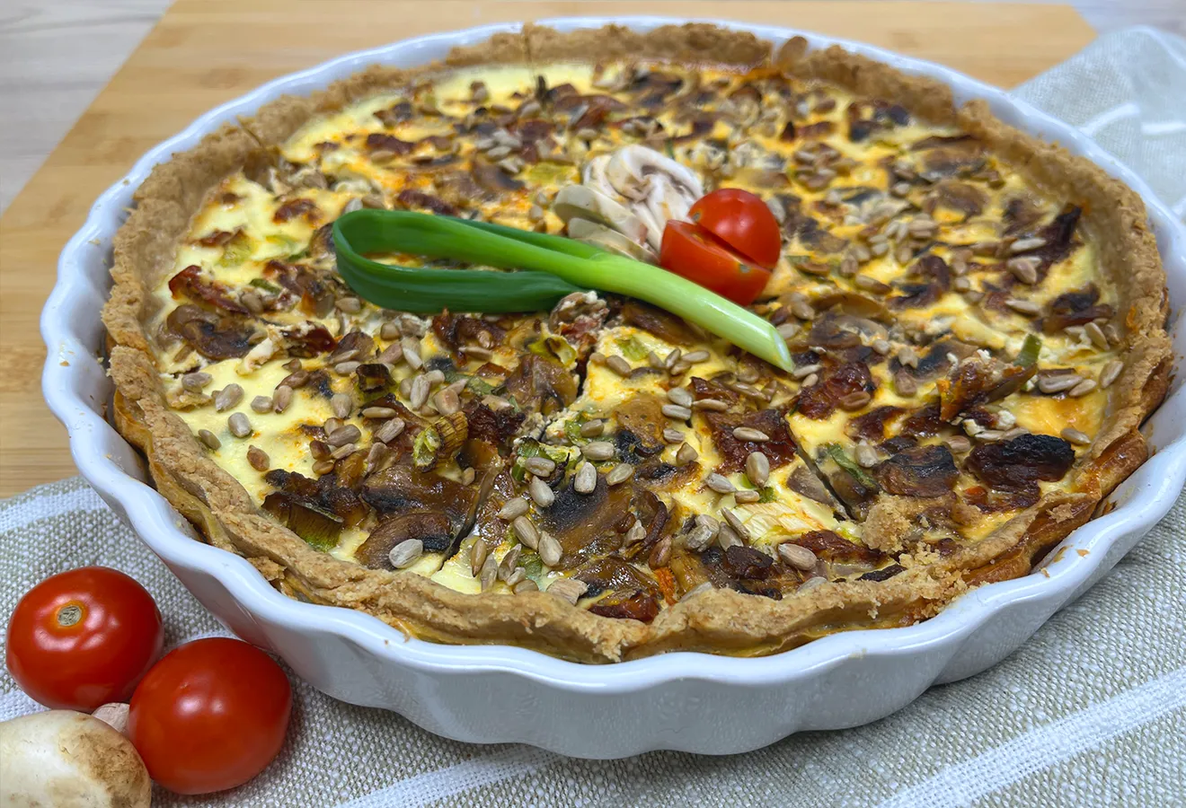 Quiche mit Pilzen, Frühlingszwiebeln und Tomaten in einer weißen Quicheform