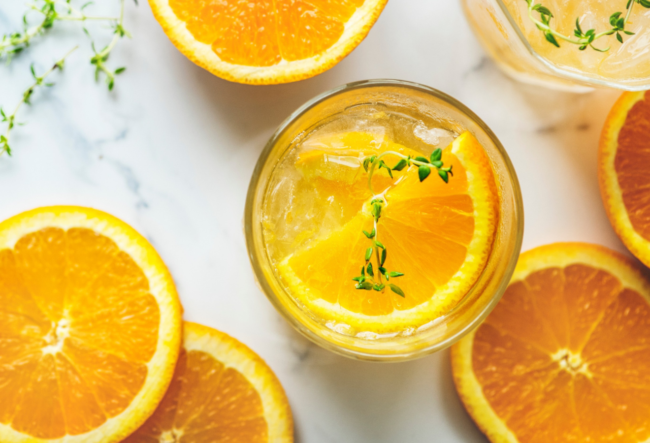 Ingwer-Orangen-Eistee in einem Glas mit Orangenscheiben, daneben weitere Orangenscheiben